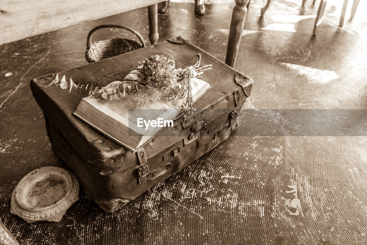 High angle view of old suitcase with open book by table on floor