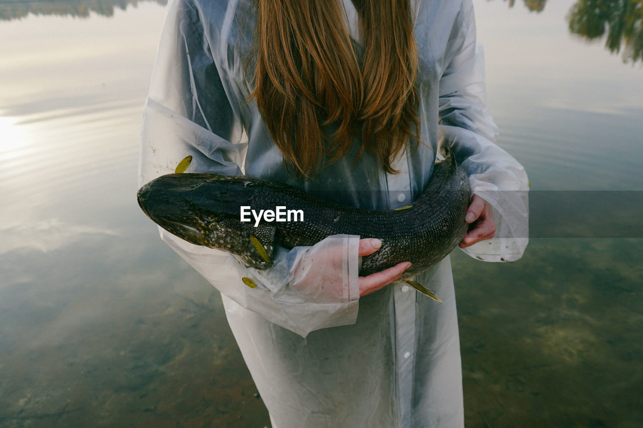 Midsection of young woman holding fish while standing in lake