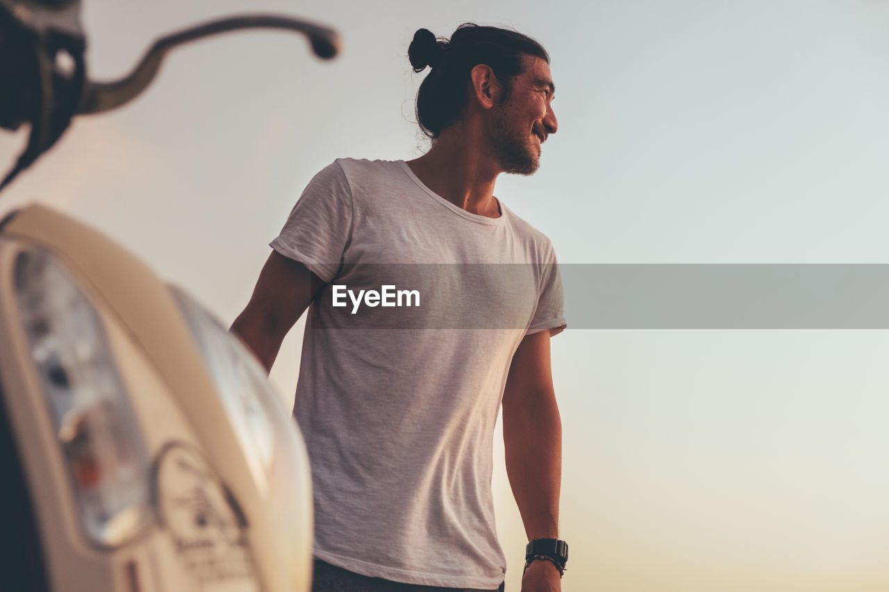 Positive man with motorbike standing at seaside