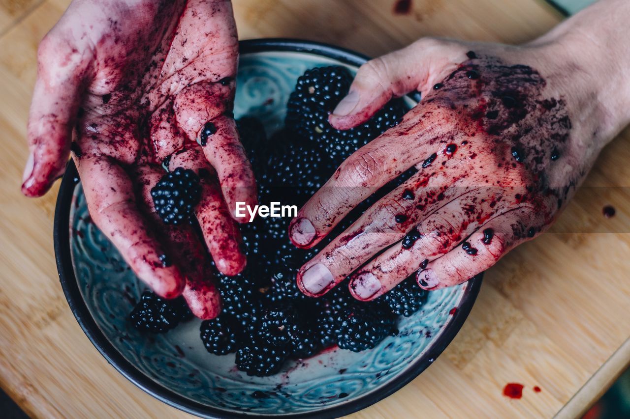 Cropped image of dirty hands holding blackberries in plate