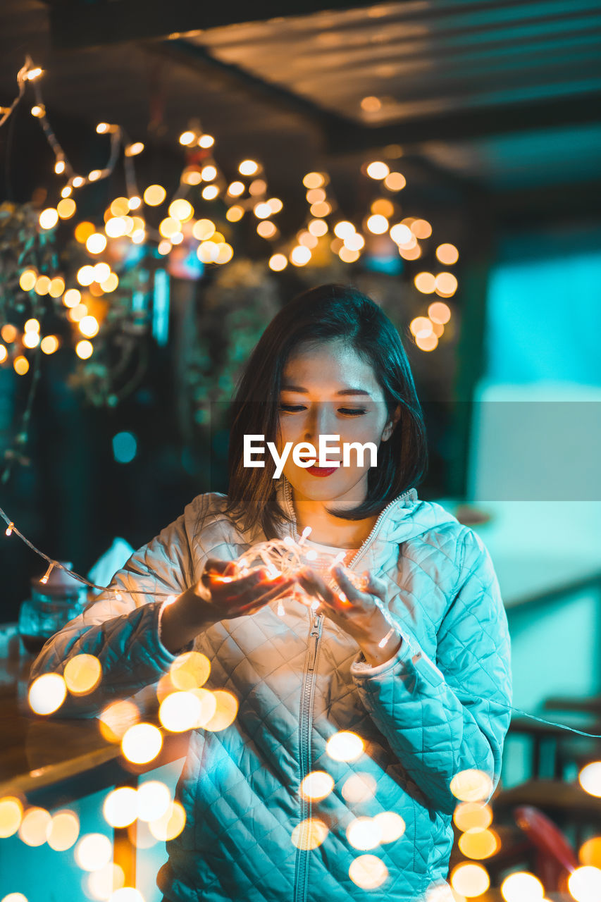 Young woman holding illuminated lighting equipment at night