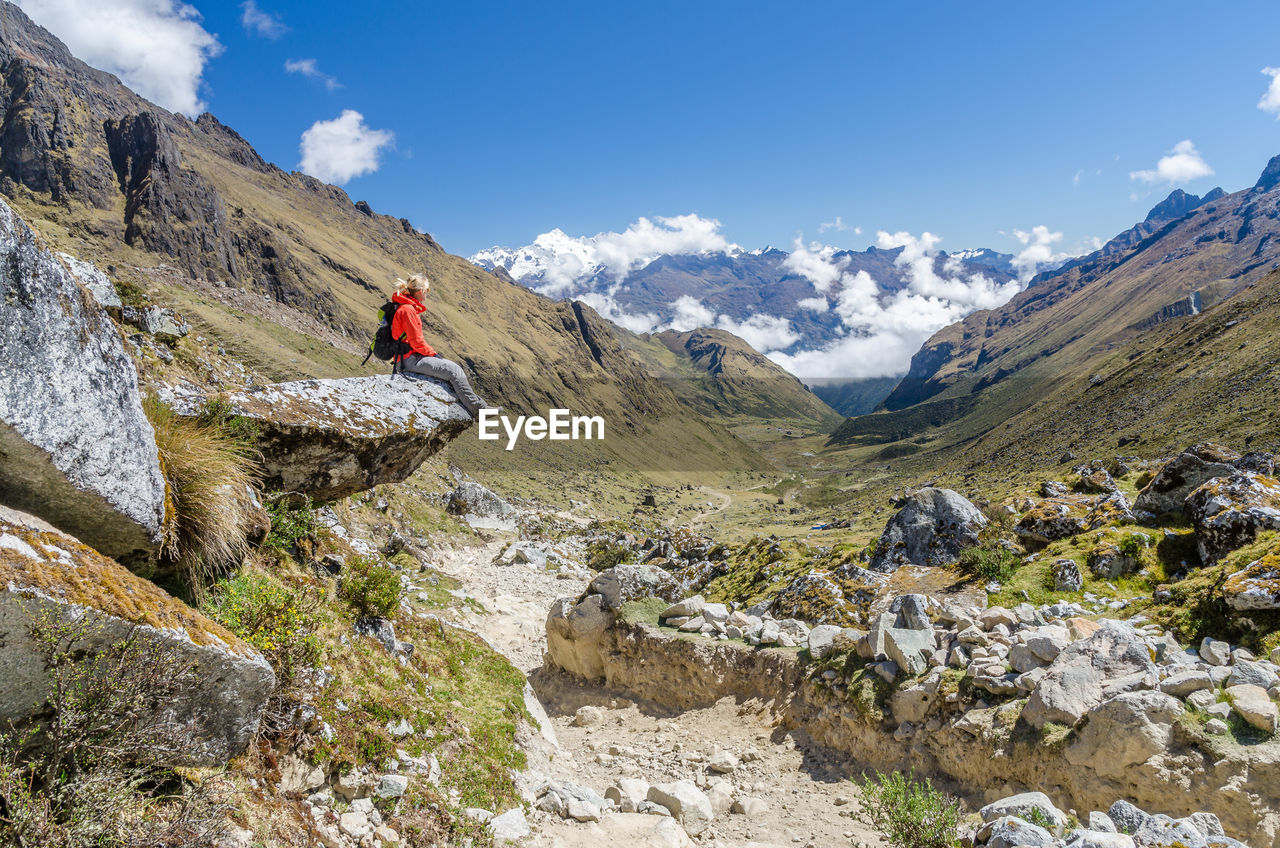 Side view of hiker relaxing on rock at mountain against blue sky