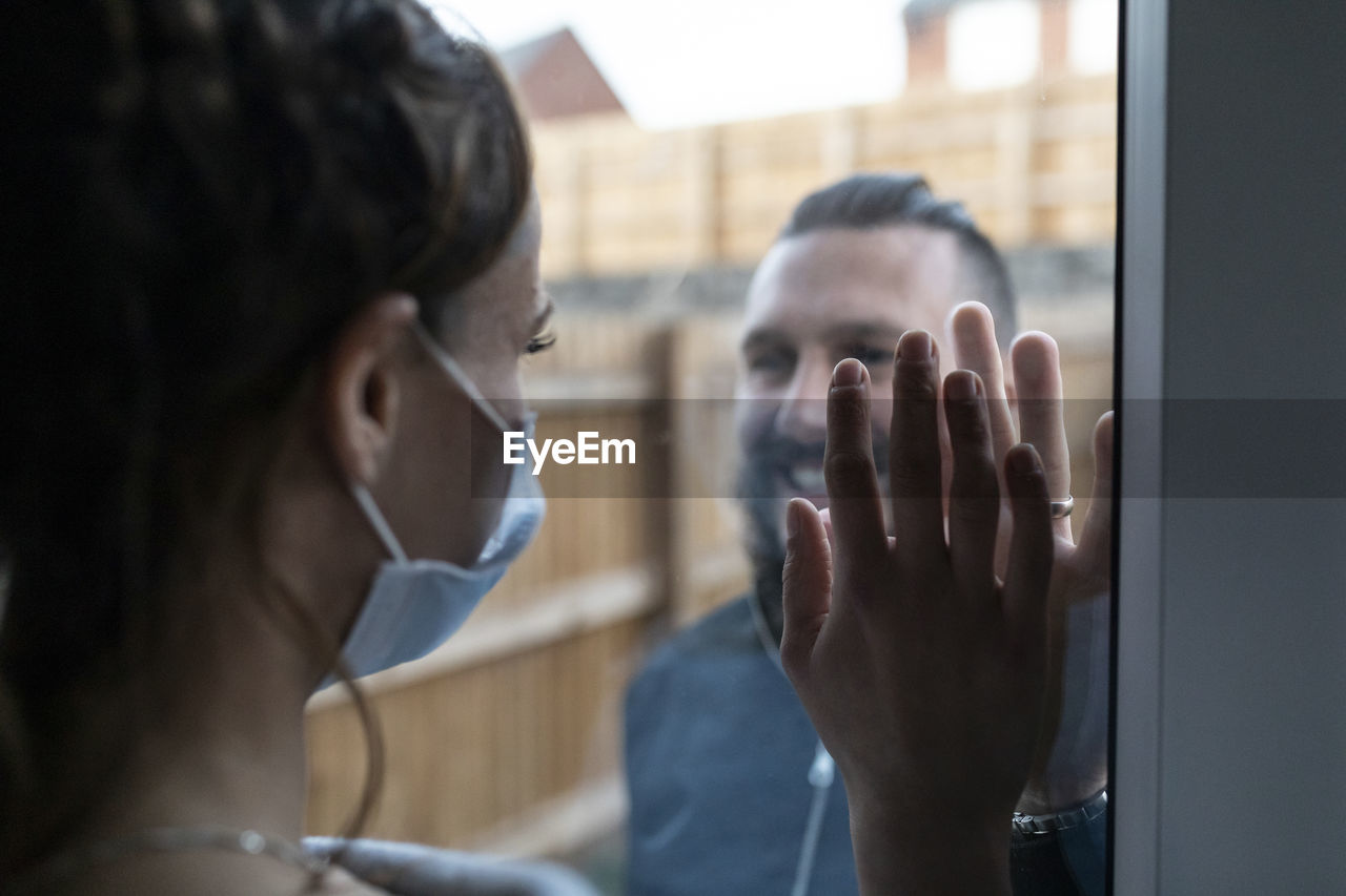 Couple touching hands from window glass during covid-19 pandemic