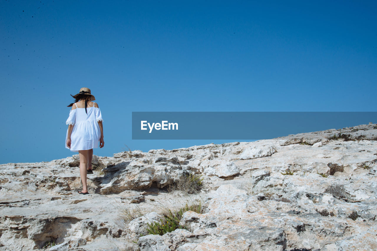 Rear view of woman walking on rock formation against clear sky