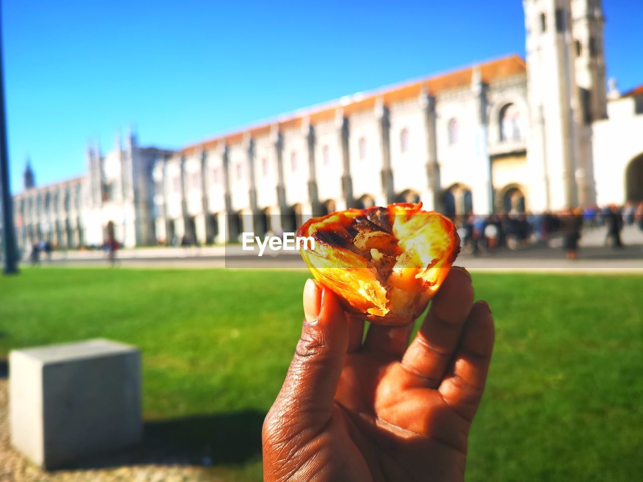 CLOSE-UP OF HAND HOLDING ICE CREAM AGAINST BUILDING