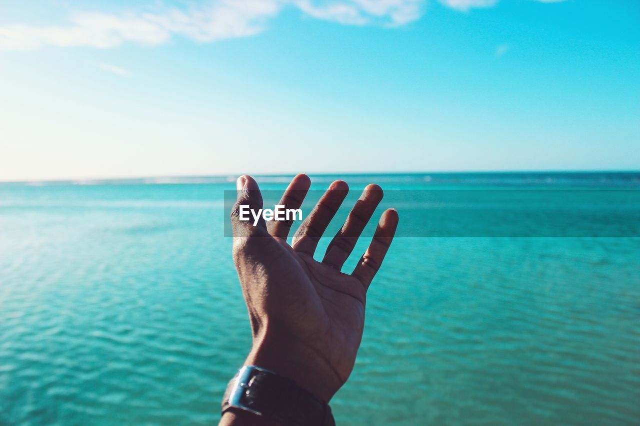 View of hand reaching towards sea