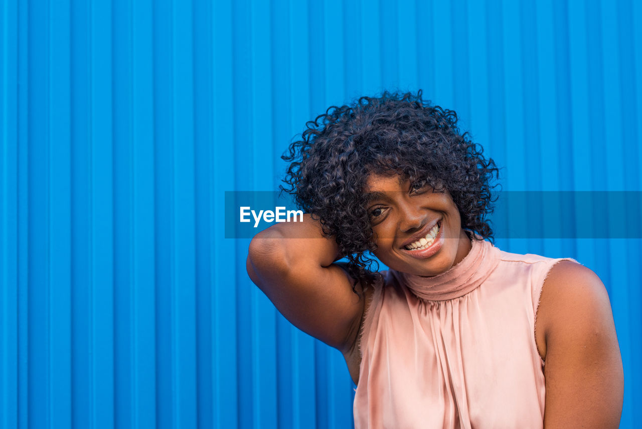 Portrait of smiling young woman standing against blue wall