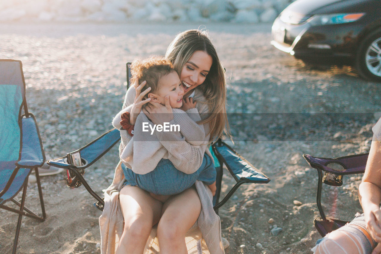 Smiling mother and daughter sitting on chair outdoors