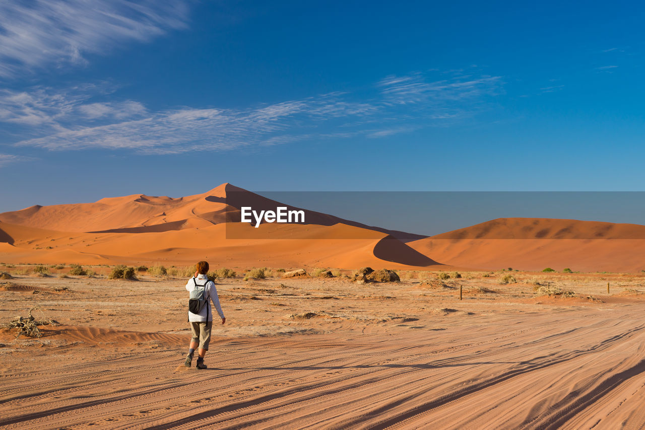 Rear view of hiker walking in namib desert against sky during sunny day