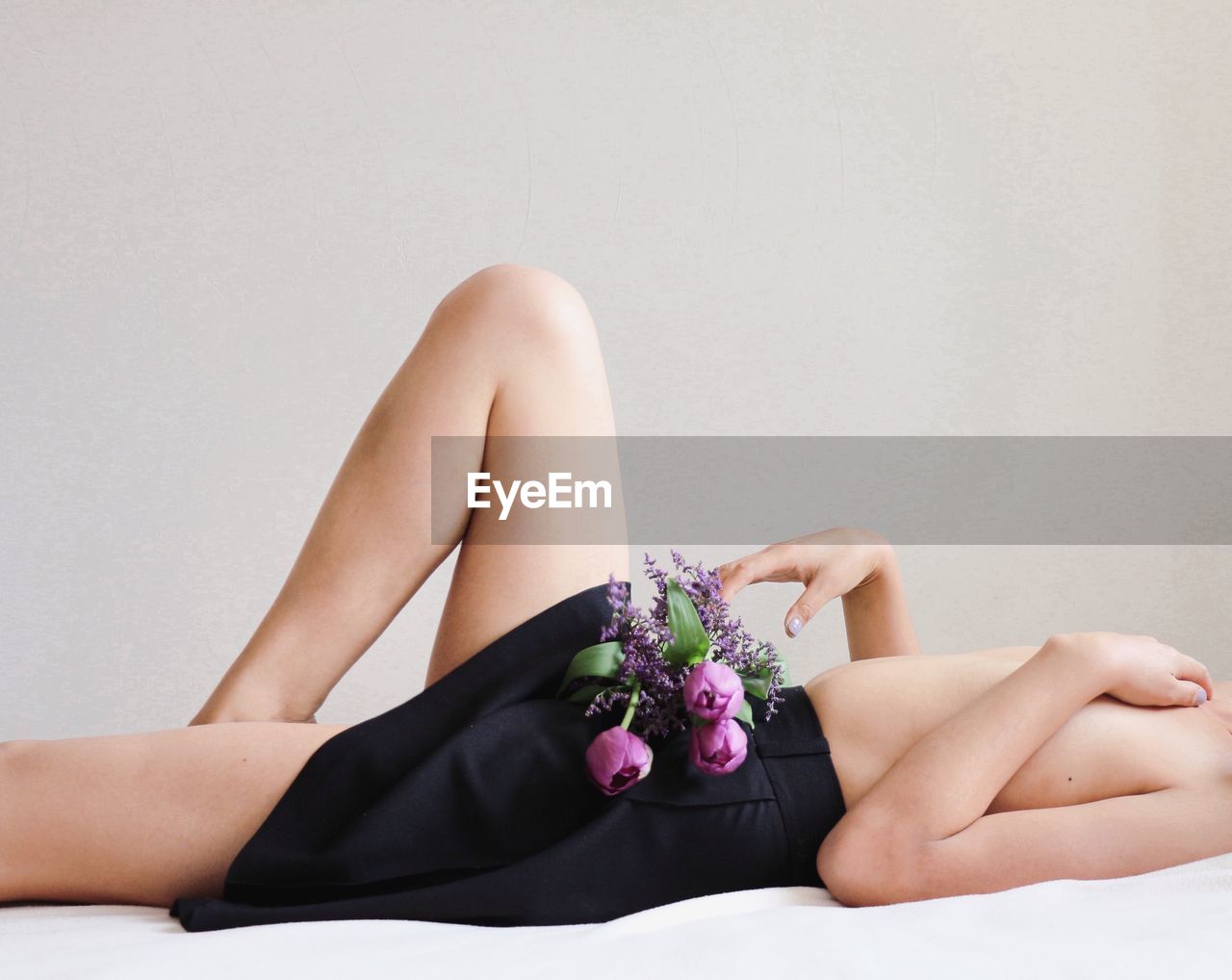 Midsection of topless woman lying on bed with flowers against beige background