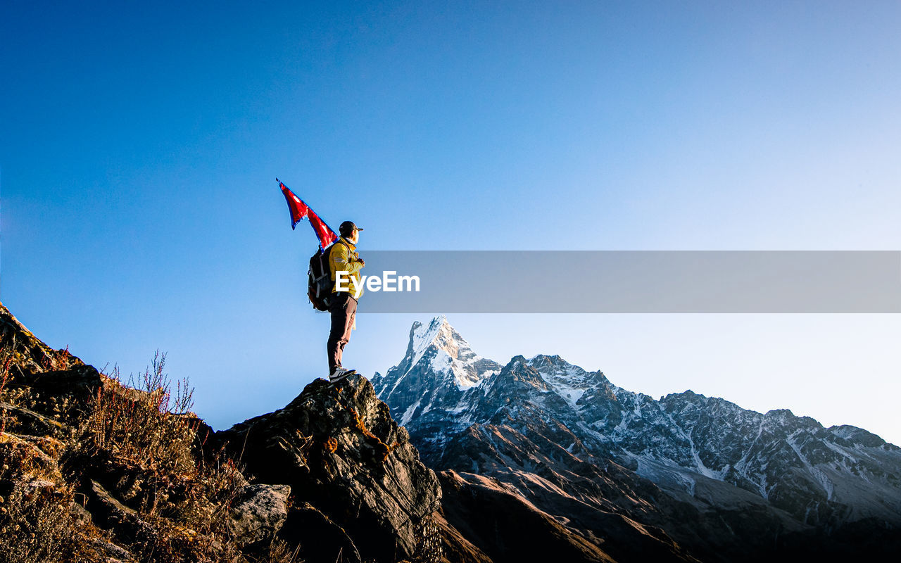 Man holding nepali flag while standing on mountain against clear blue sky