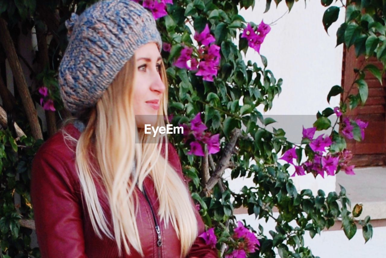 PORTRAIT OF BEAUTIFUL YOUNG WOMAN LOOKING AT FLOWERING PLANT