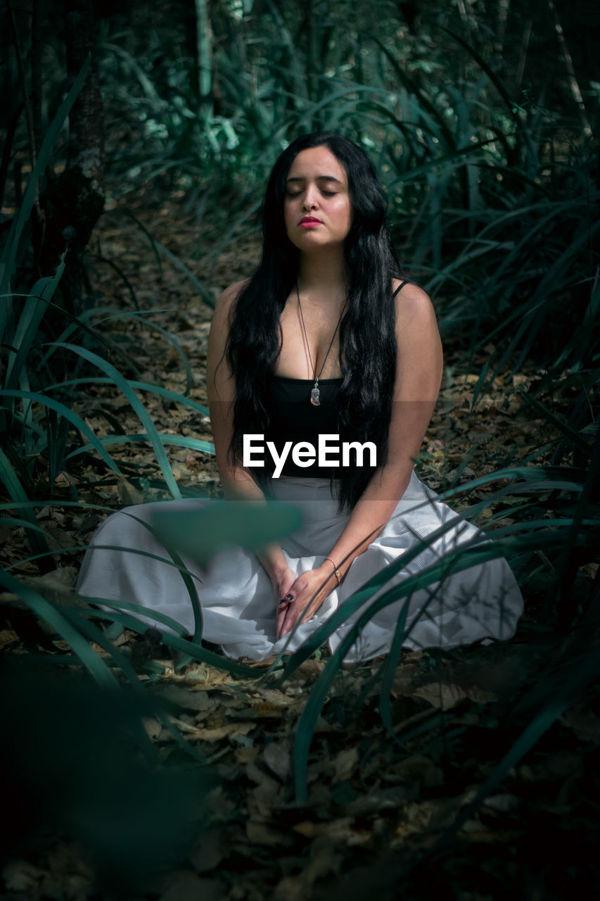 Woman with eyes closed mediating on land in forest