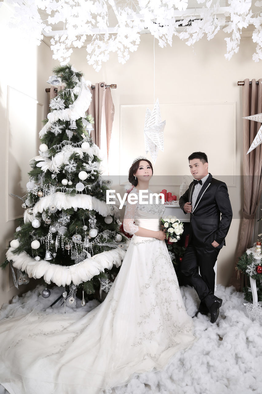 Bride and groom standing against christmas tree at home