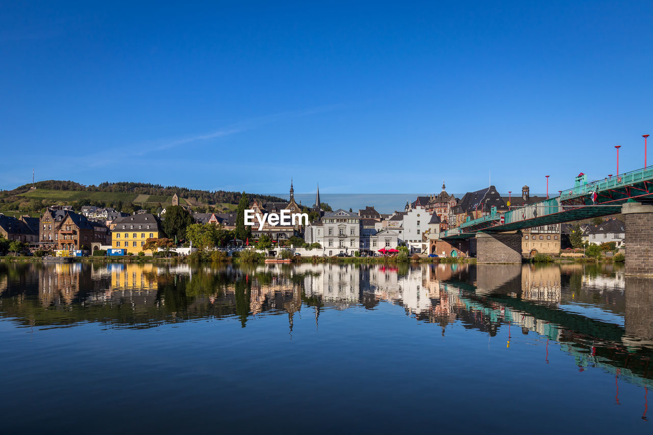 Buildings by river against blue sky