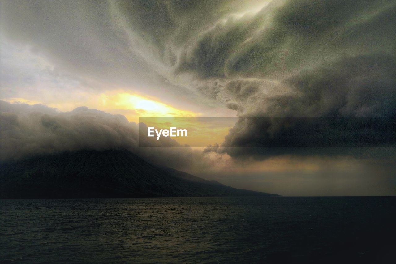 SCENIC VIEW OF SEA AND MOUNTAINS AGAINST DRAMATIC SKY