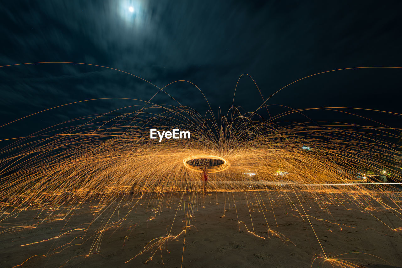 Person spinning wire wool against sky at night