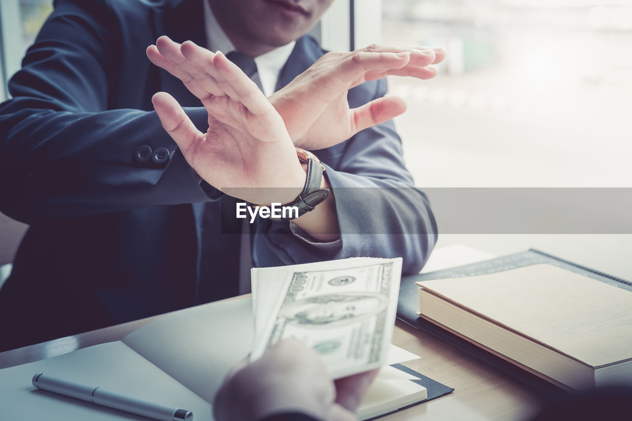 Cropped hand of person bribing businessman at desk in office