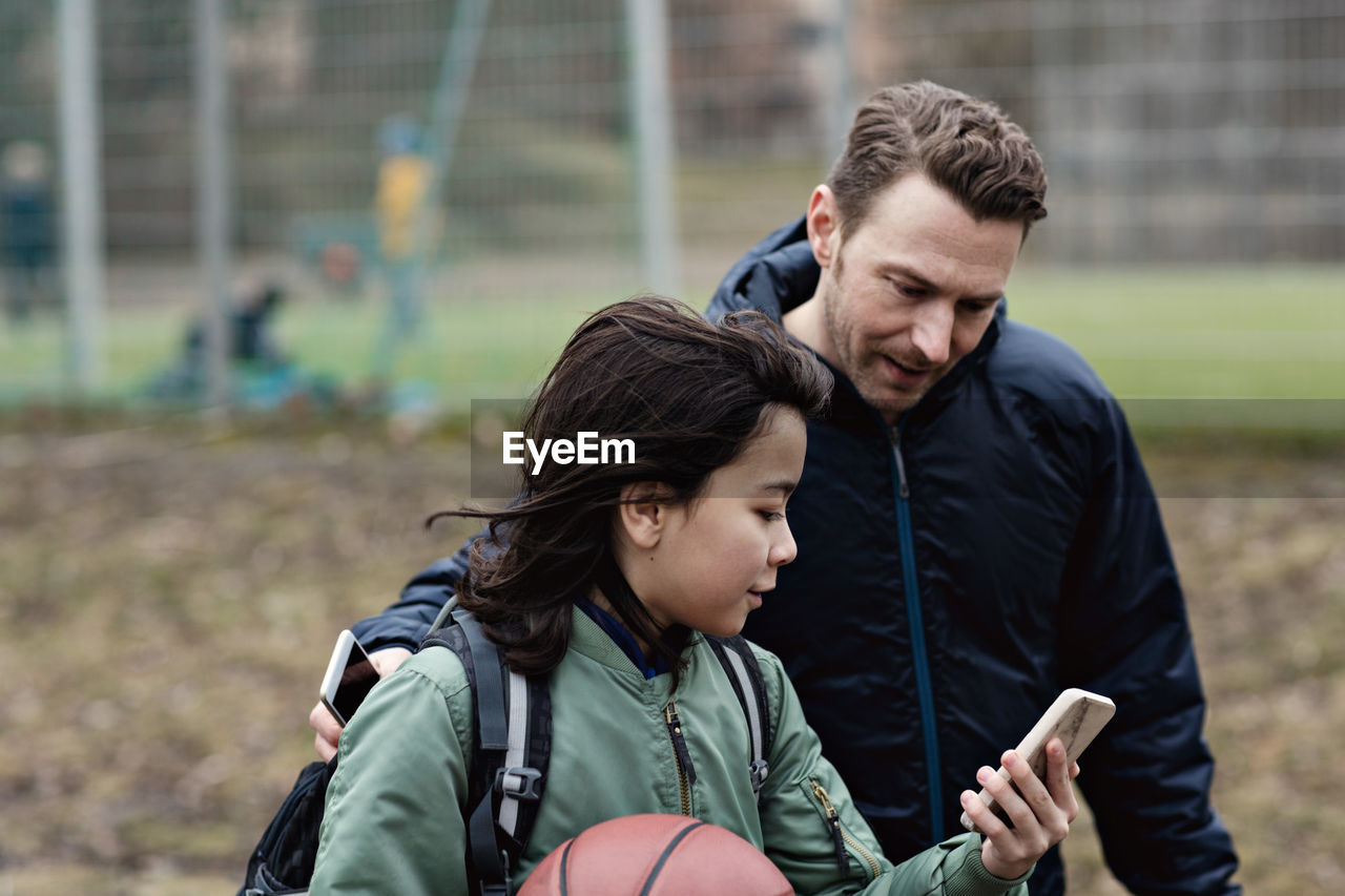 Son showing his smart phone to father while standing by sports court