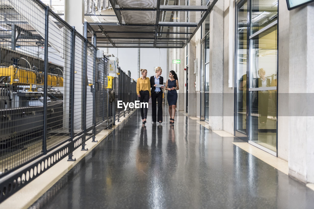 Three women with tablet walking and talking in factory shop floor