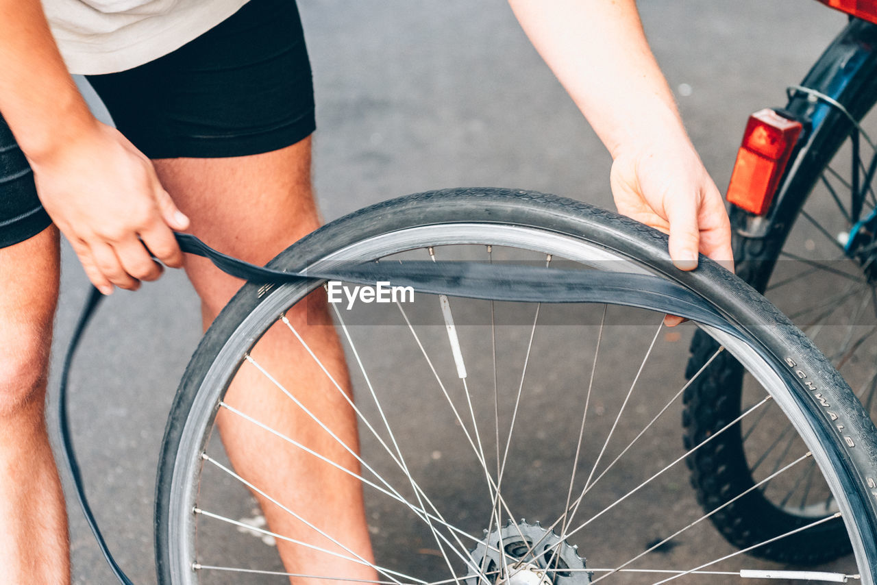 Cropped image of man repairing flat tire of bicycle on street