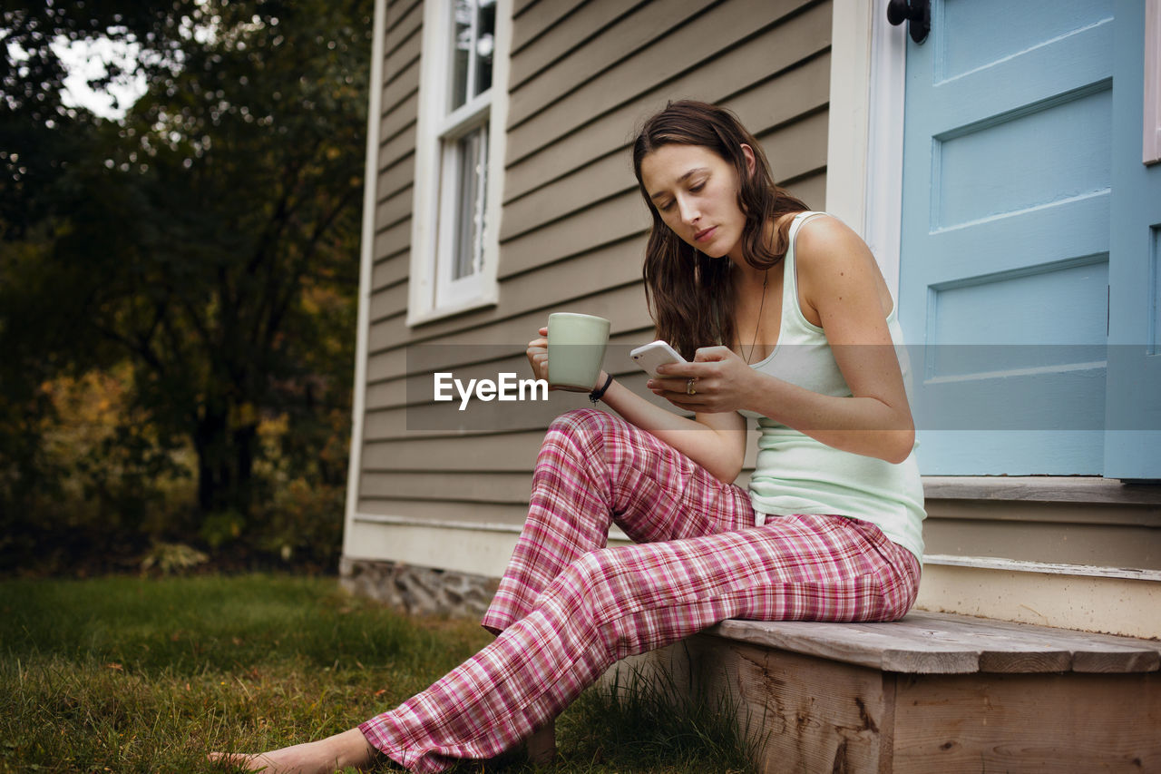 Young woman using smart phone while sitting outside house