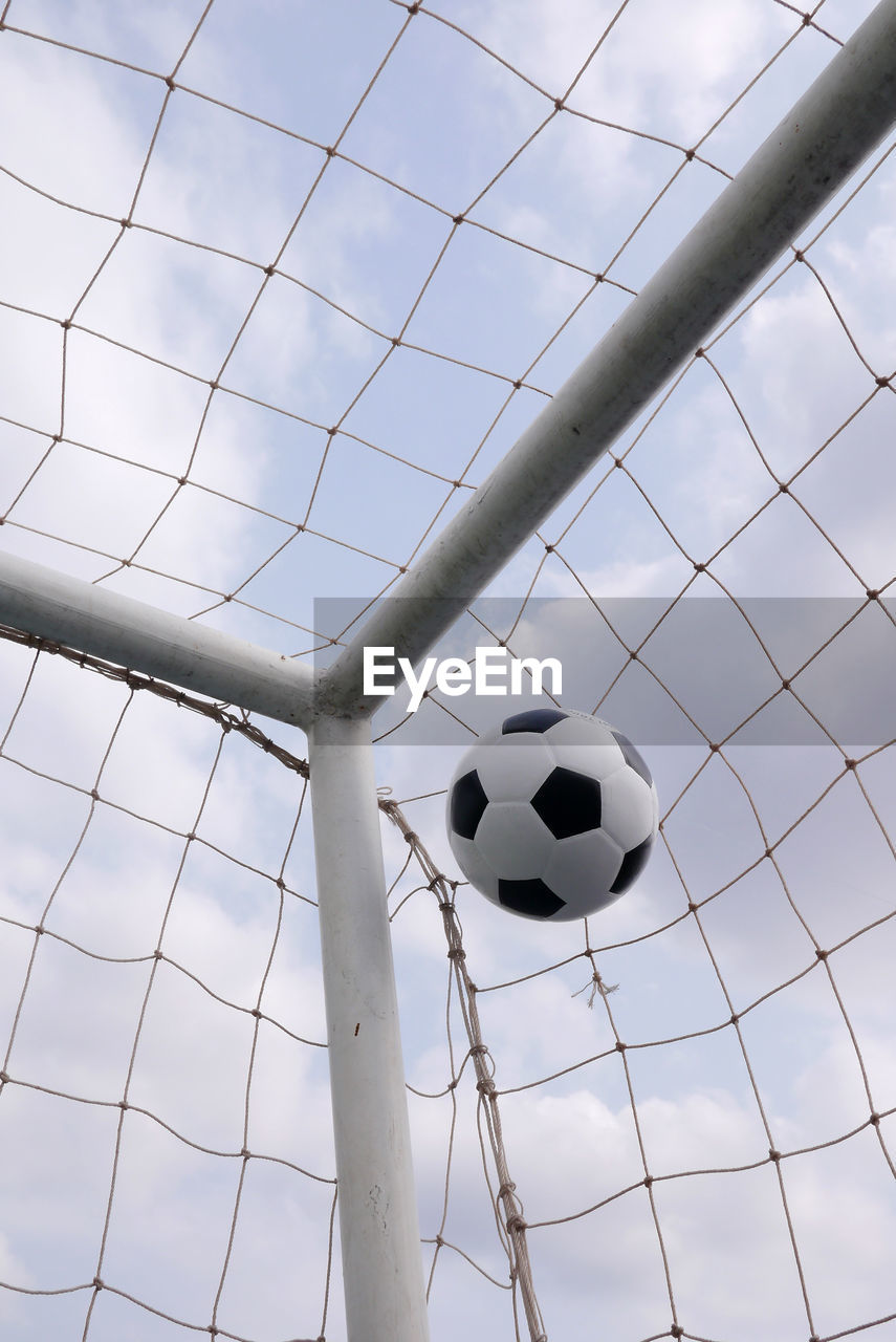 Low angle view of soccer ball on net against sky