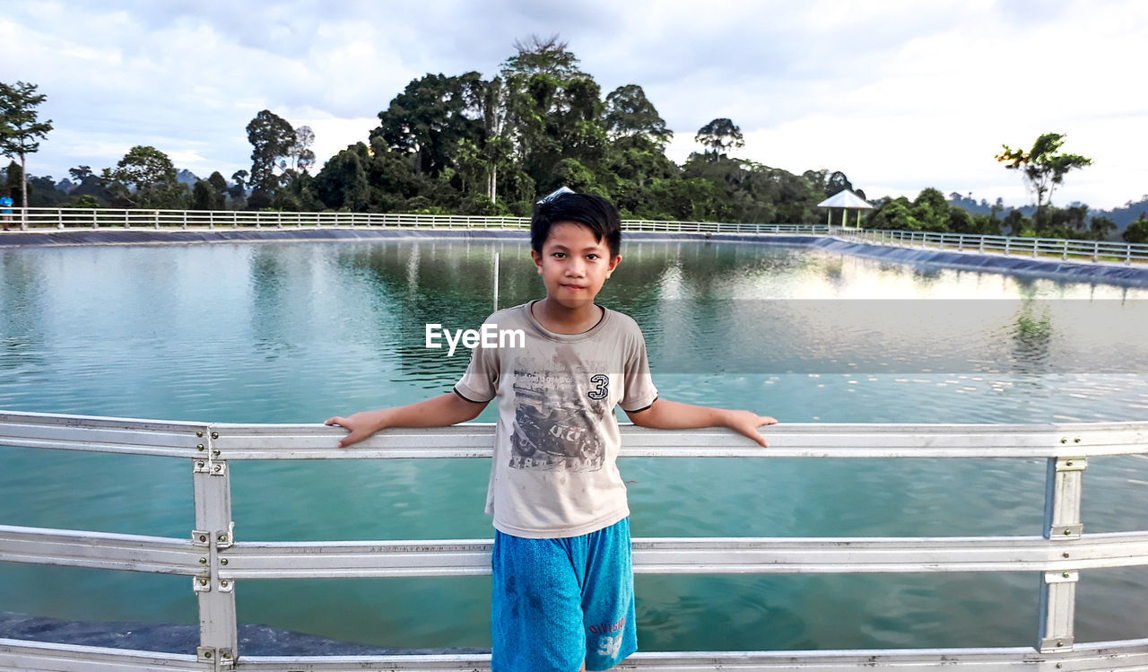 Portrait of man standing by railing against lake