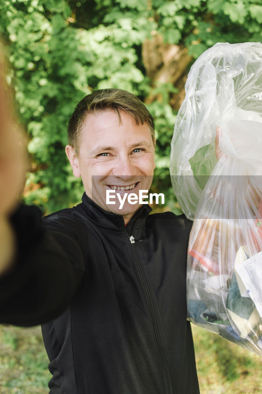 Portrait of smiling coach taking selfie with garbage bag