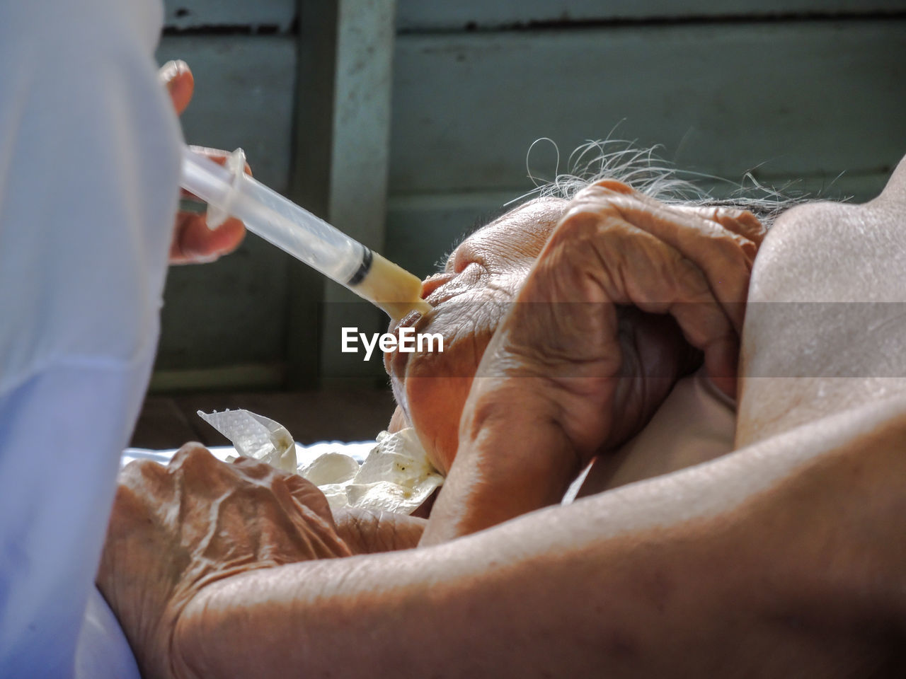 Midsection of doctor feeding senior woman through syringe 