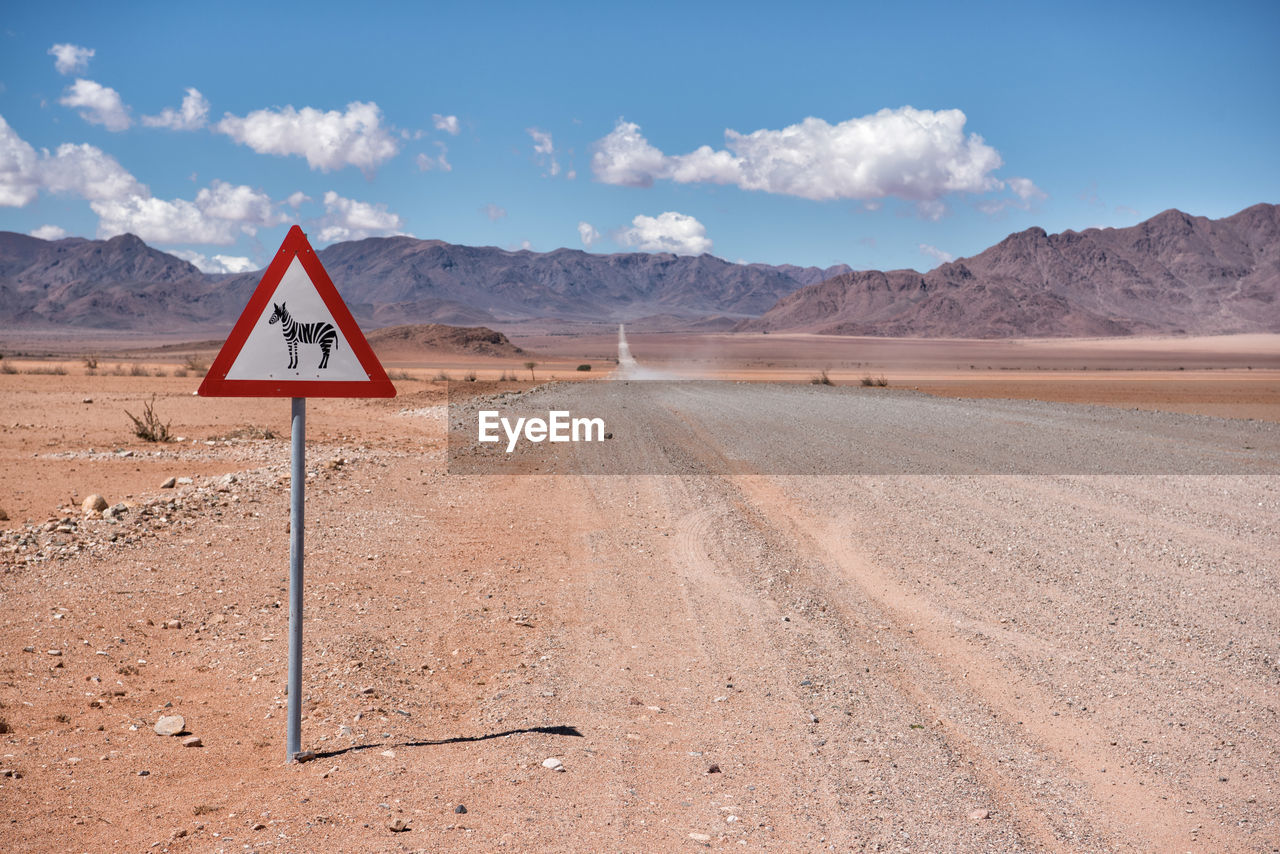 Information sign on dirt road against sky