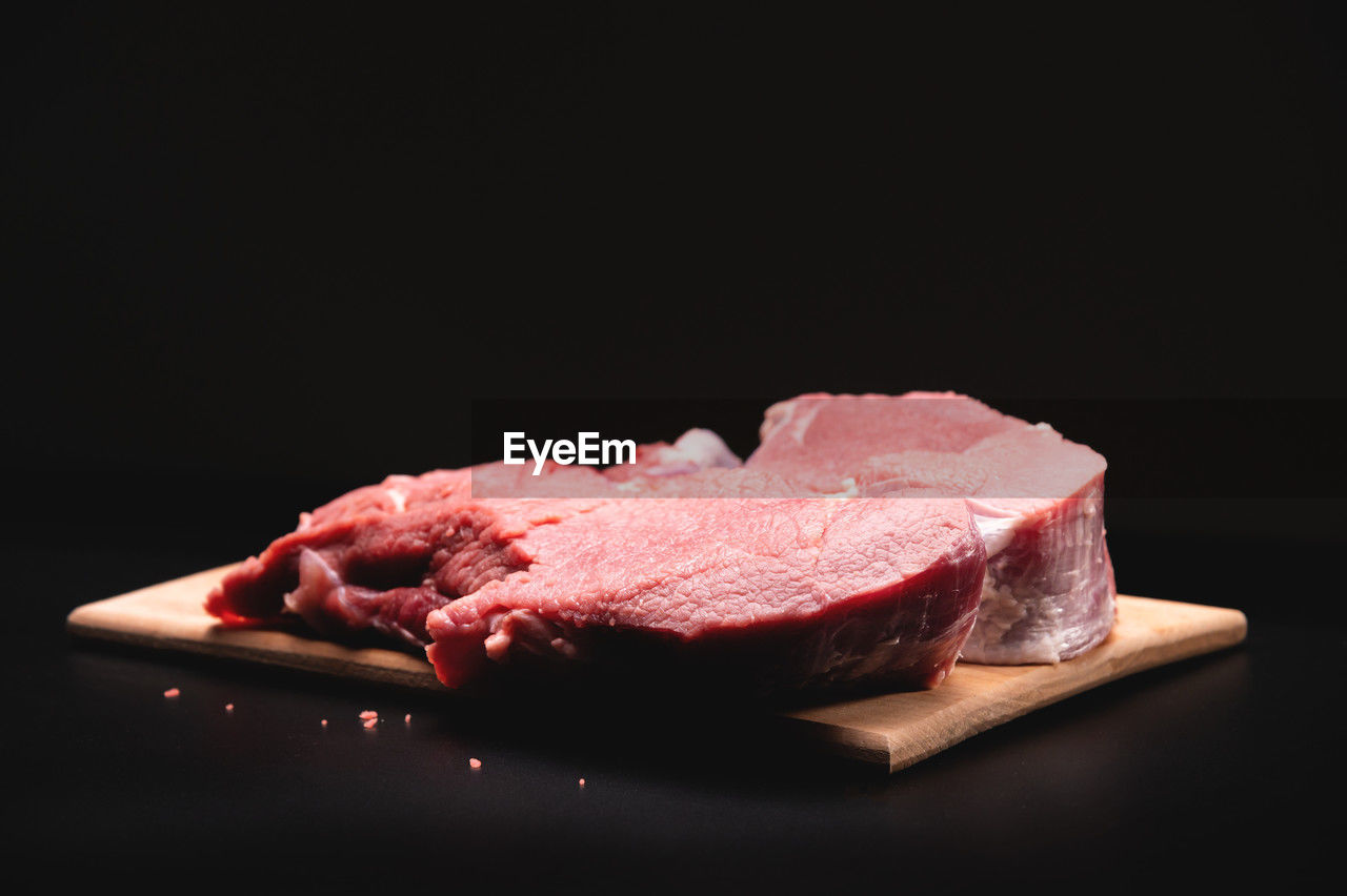 Piece of raw beef in a slice on a wooden cutting board, on a black background. procuring food