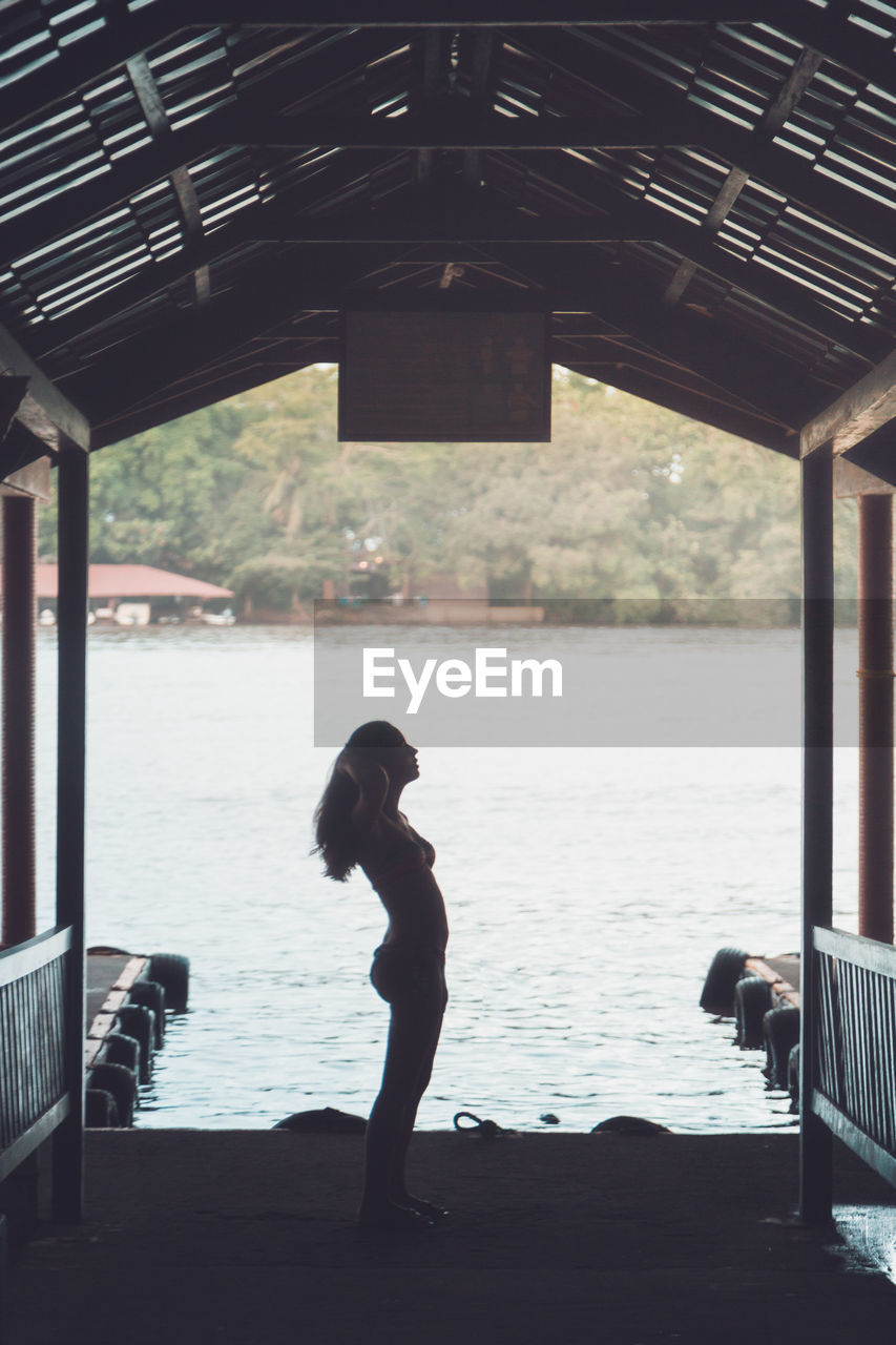 Side view of silhouette woman standing in gazebo against lake