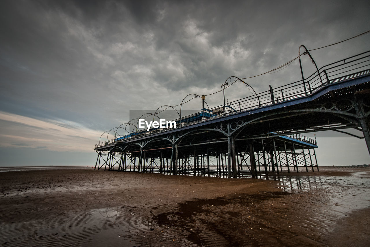 Low angle view of structure on beach against cloudy sky