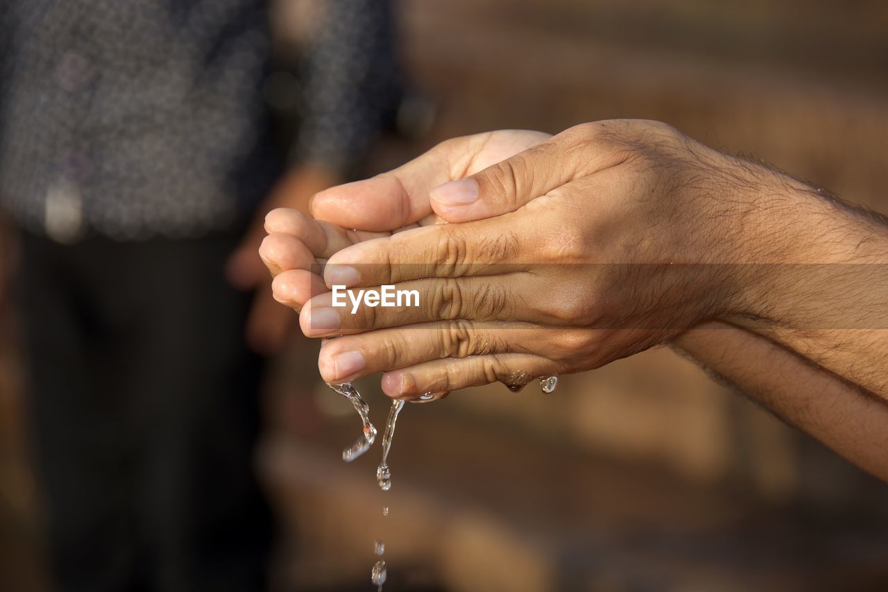 Cropped hands of man pouring water while performing prayer