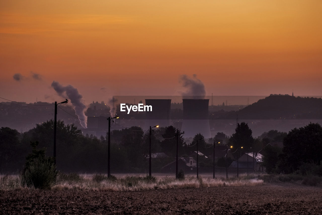 Smoke emitting from factory against orange sky