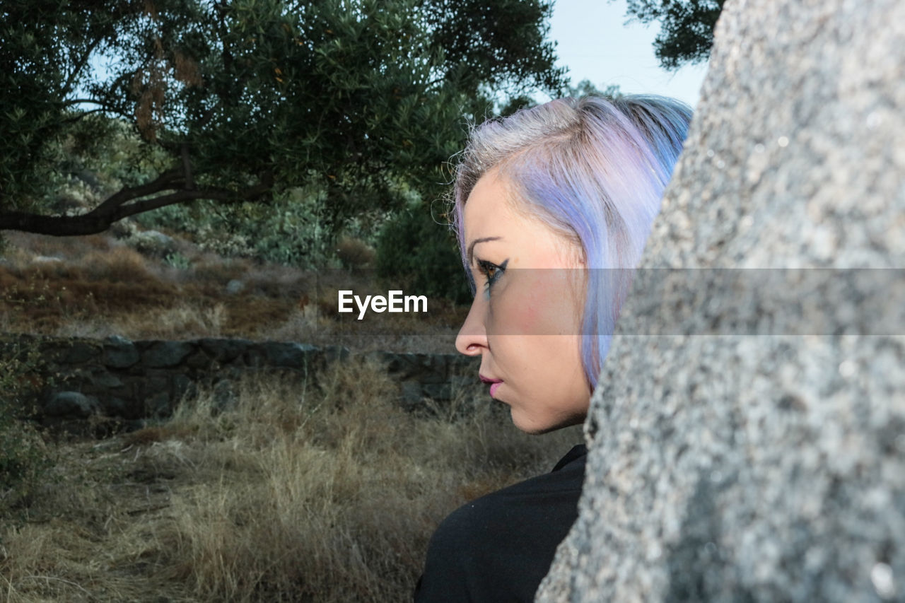 Close-up of young woman looking away against tree trunk