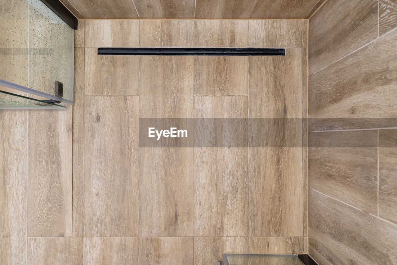 Modern black linear drain in a bathroom lined with ceramic tiles imitating wood, top view.