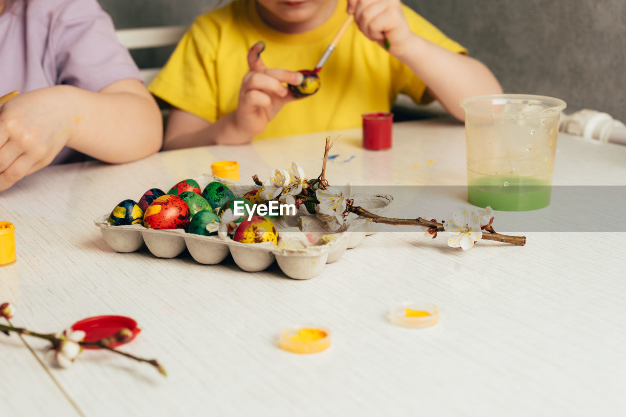 Children's hands paint eggs with a brush. painted eggs on a table with paints 