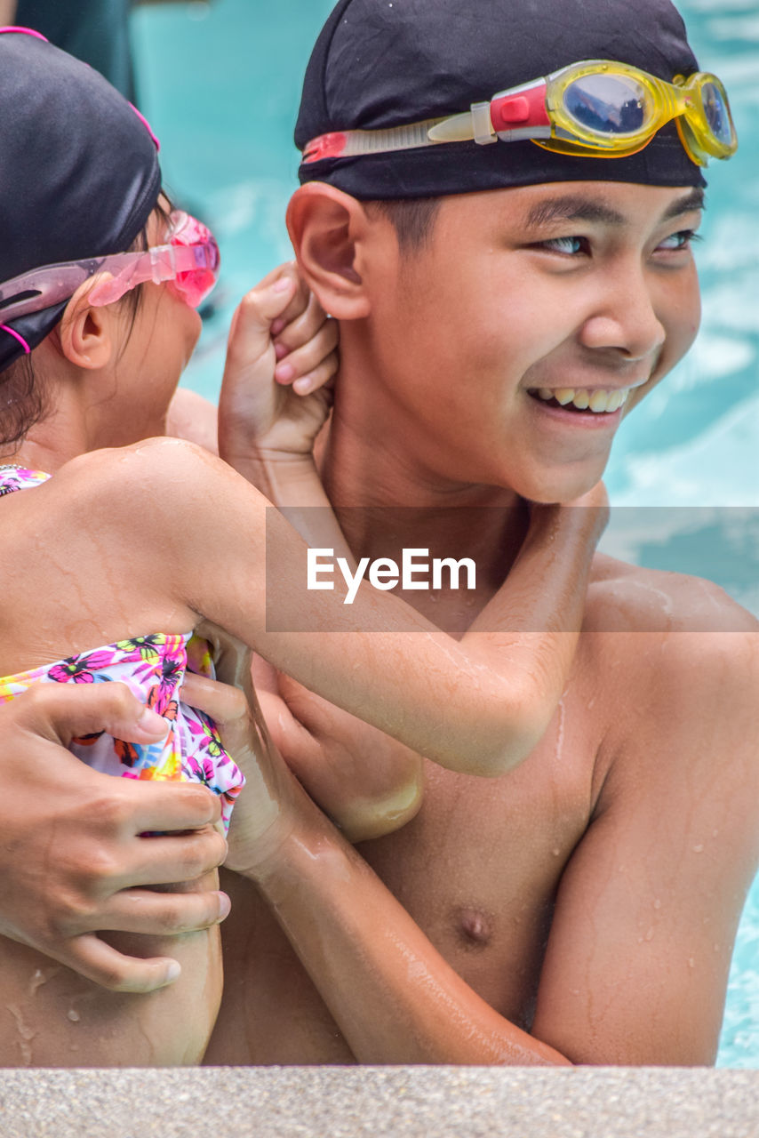 Boy with sister looking away while enjoying in swimming pool