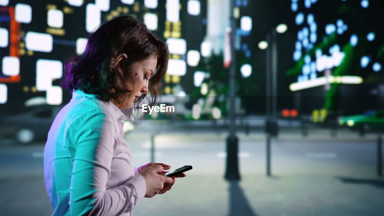 side view of young woman using mobile phone at night