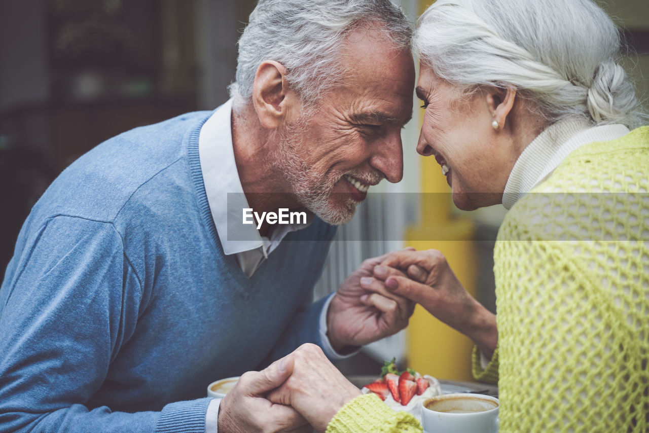 Smiling senior couple holding hands sitting at cafe