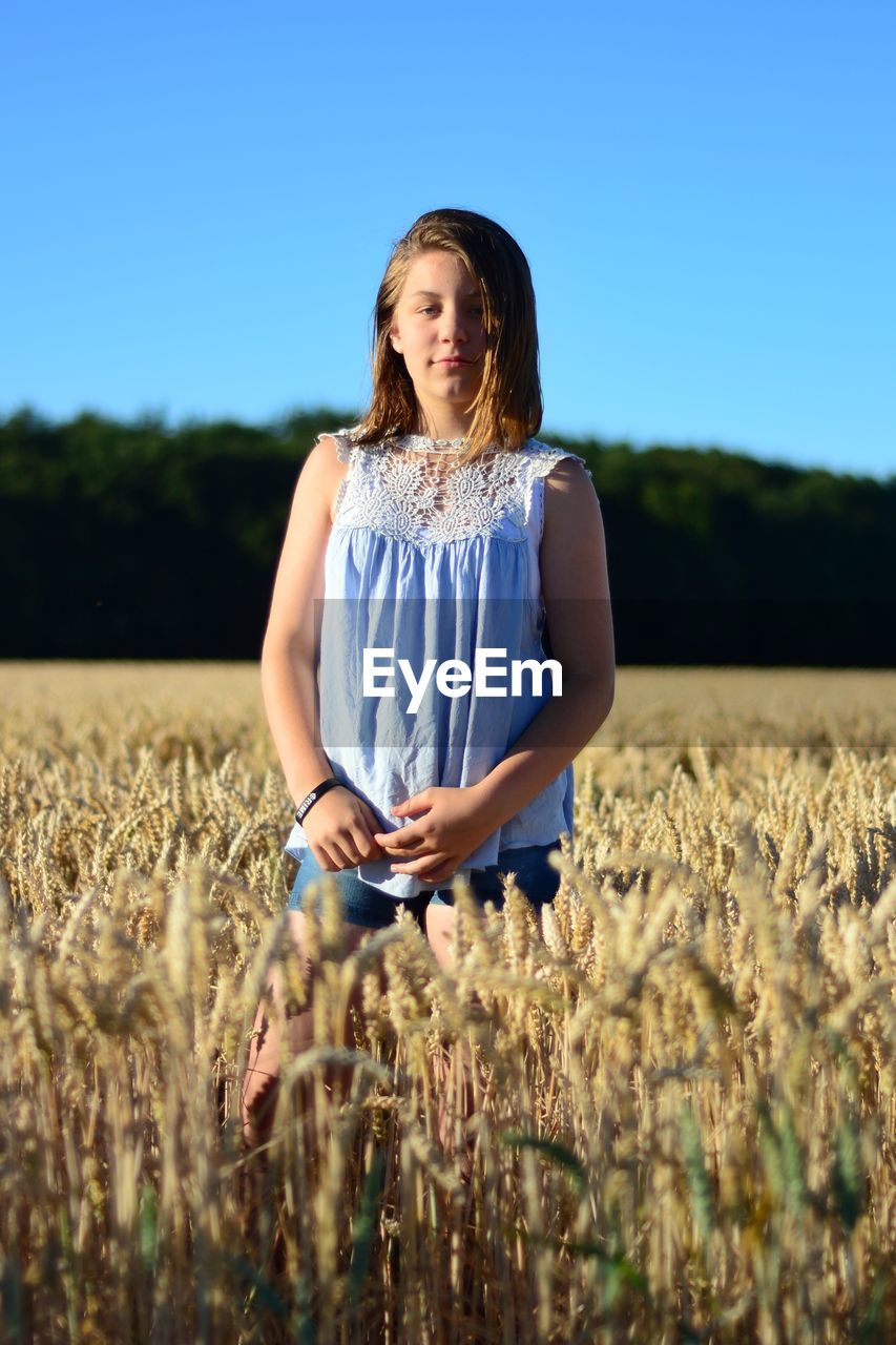 Portrait of teenage girl standing at farm against clear blue sky