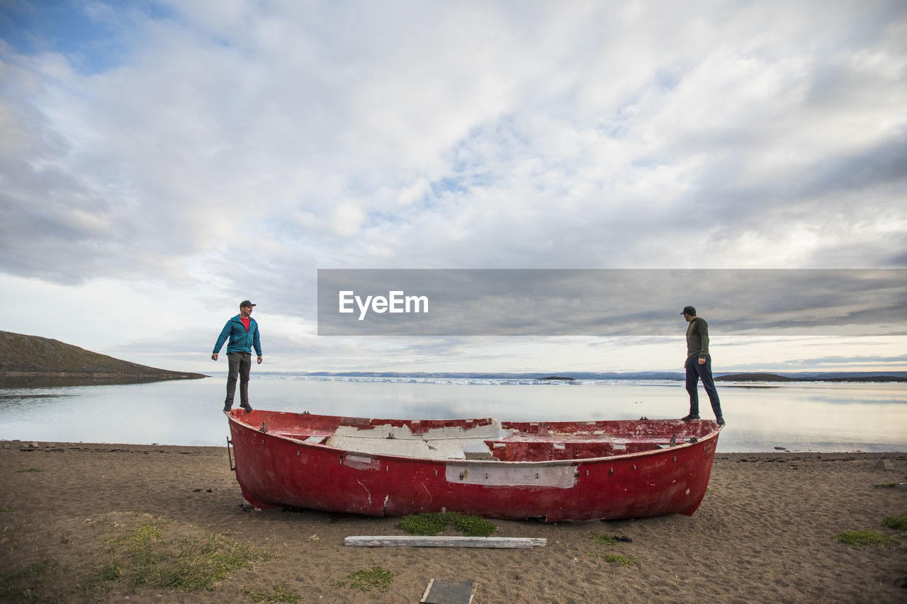 Two men stand on the edge of a retired red whaling boat.