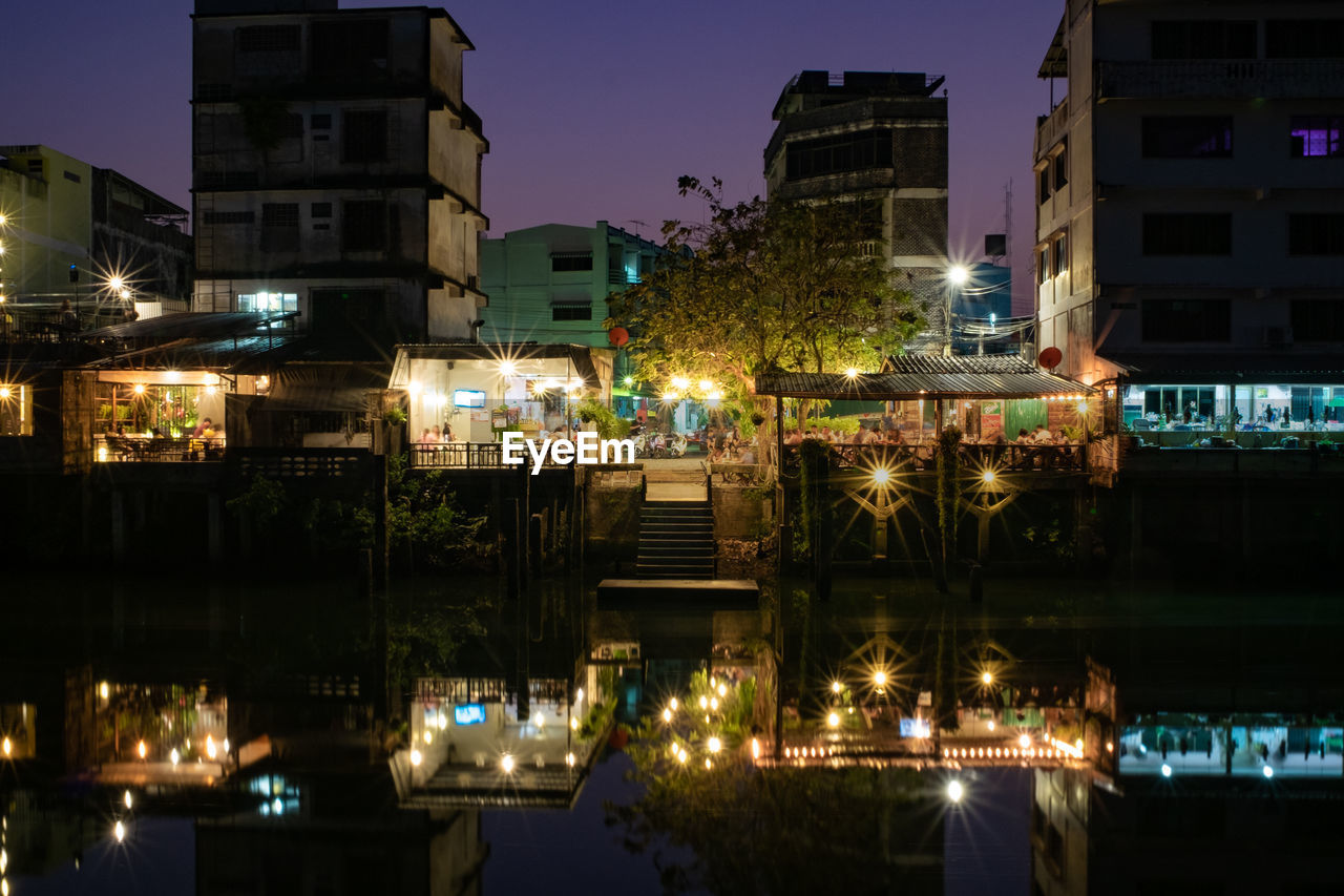 Illuminated buildings by lake against sky in city at night