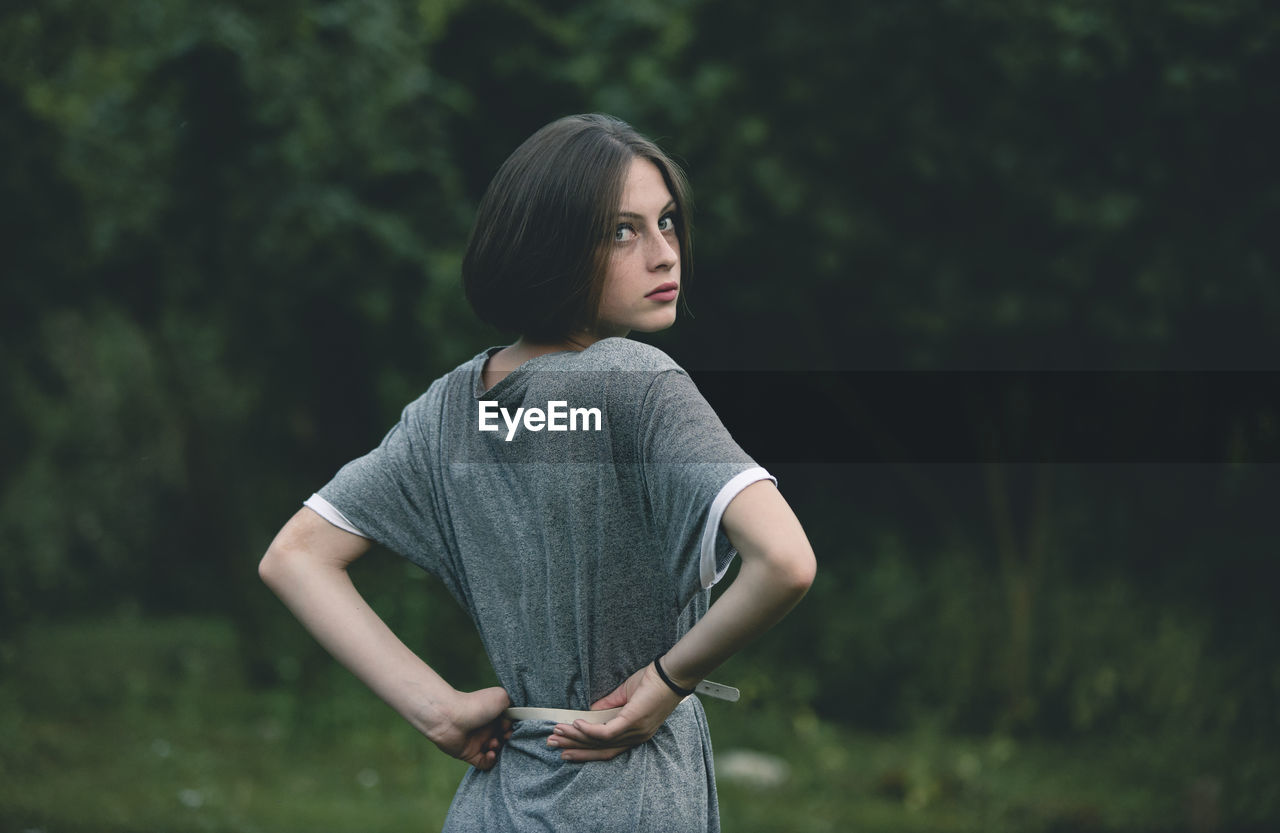 Young woman looking away while standing against trees