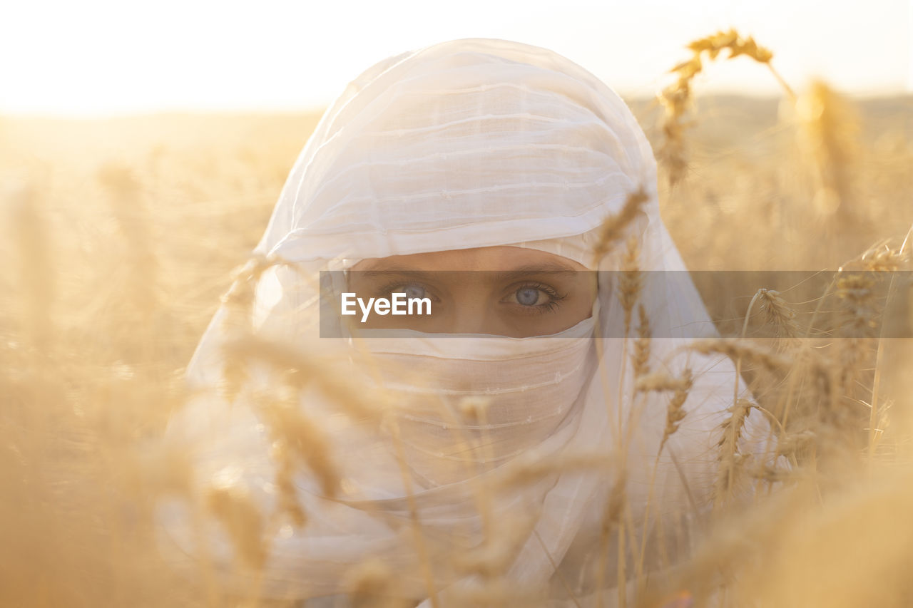 Blue-eyed woman with her face covered in a wheat field
