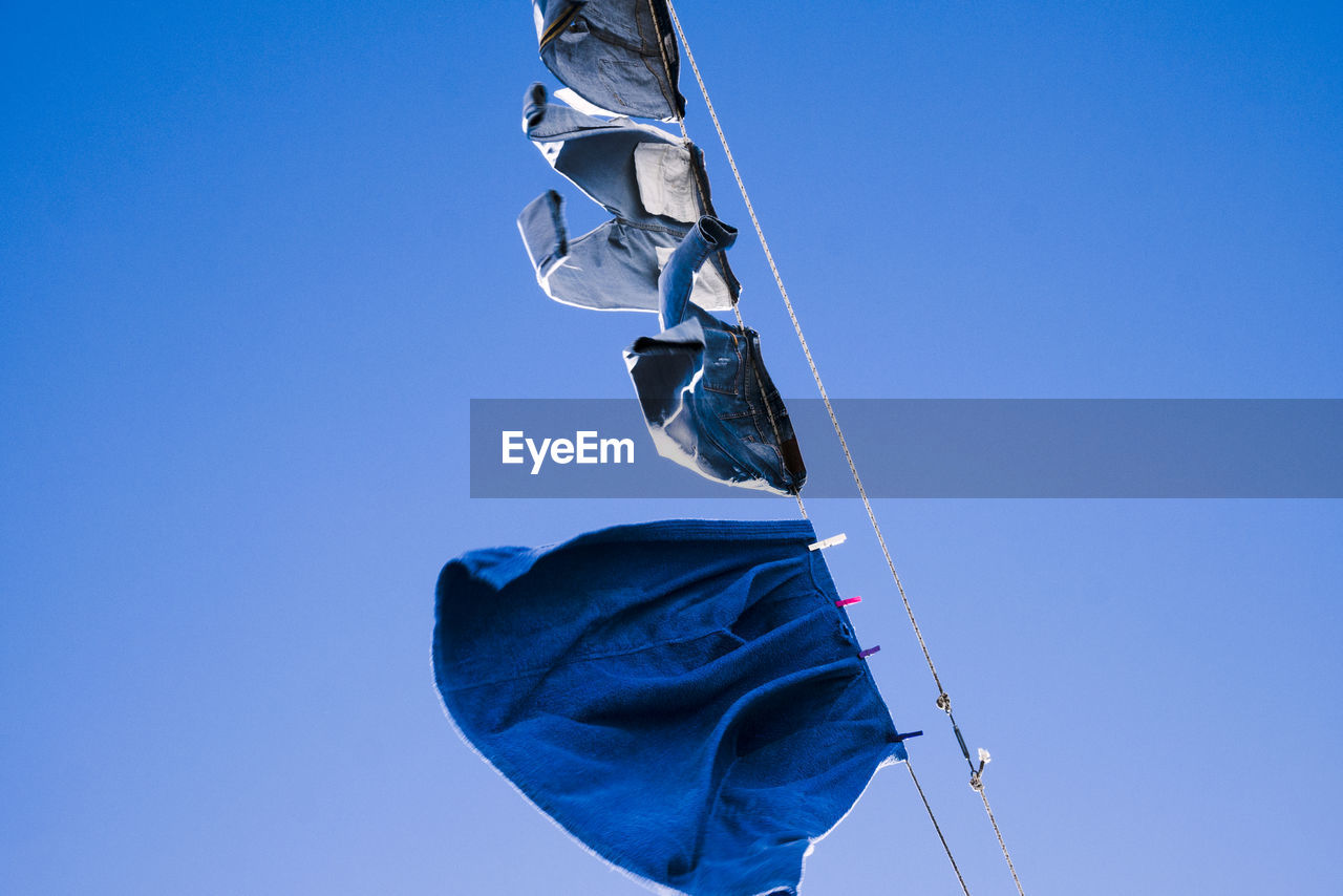 Low angle view of laundry hanging on clothesline against clear blue sky