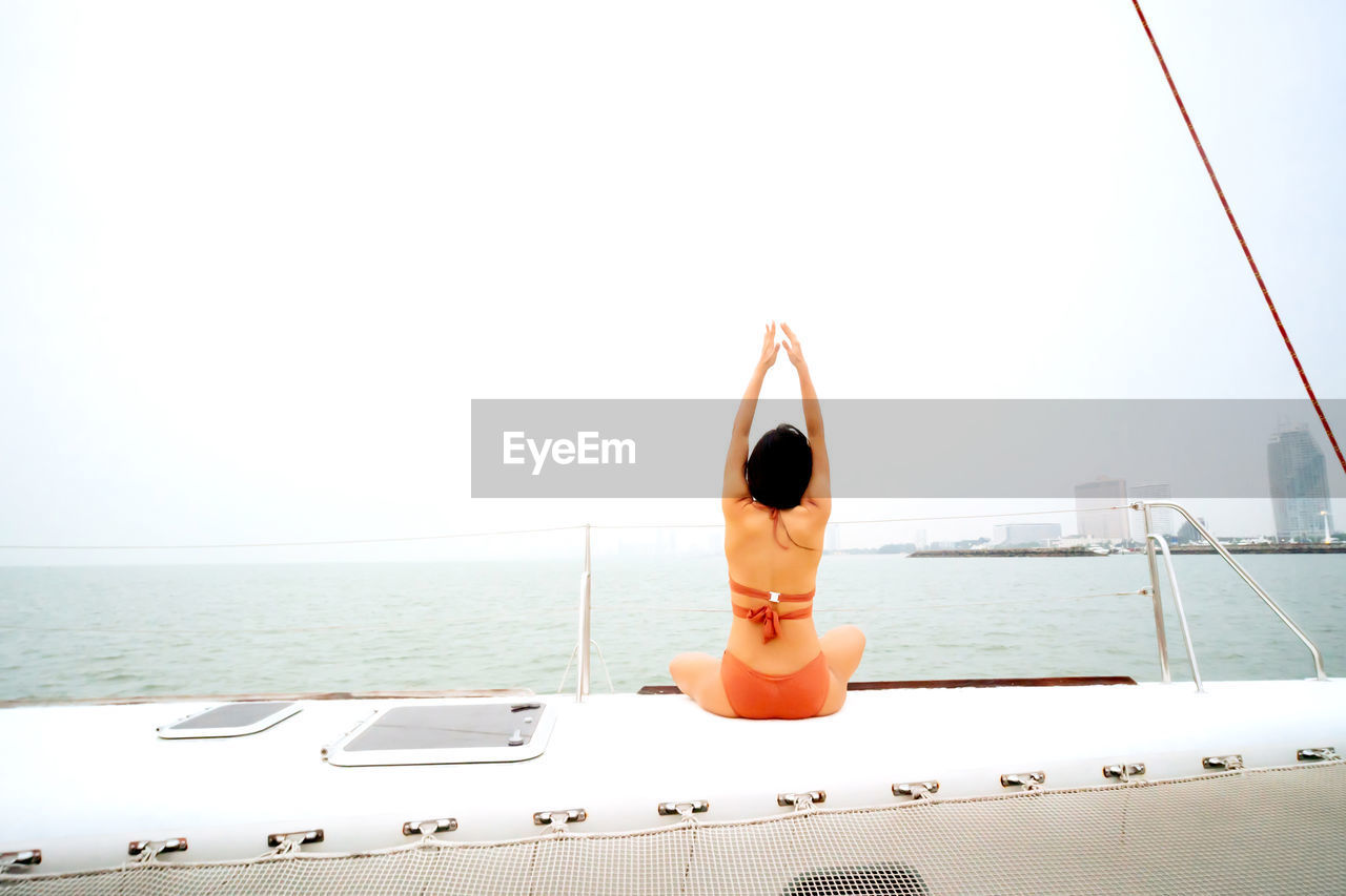 REAR VIEW OF WOMAN SITTING IN BOAT AGAINST SKY