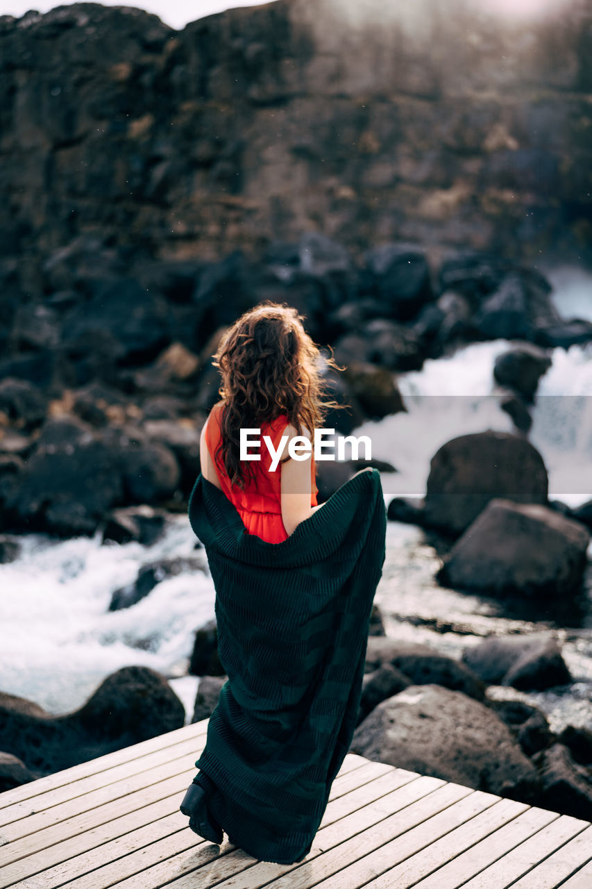 REAR VIEW OF WOMAN SITTING ON WOOD